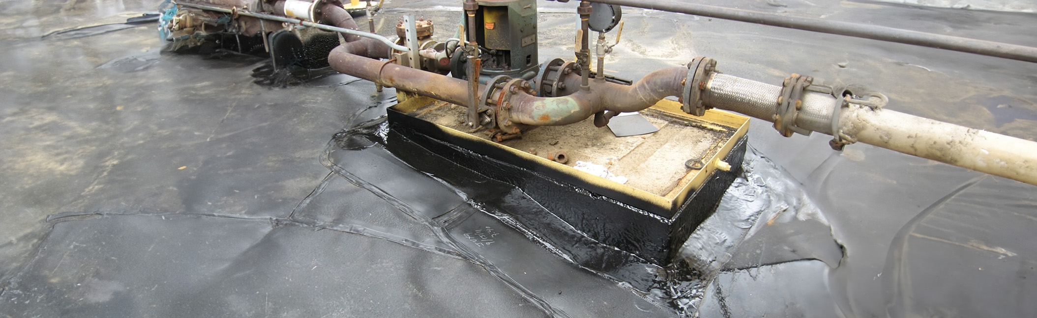 A close-up of industrial equipment sealed with PolySeam containment liner, featuring pipes and a pump on a platform.