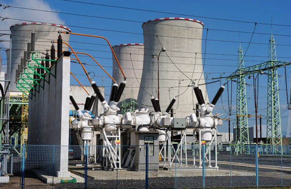 An electric power substation with cooling towers, electrical equipment, oil containment systems, and transmission lines under a clear blue sky.